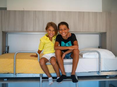 Deux enfants souriants assis sur un lit superposé.