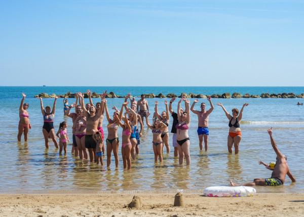 Gruppo felice in mare, braccia alzate, sole estivo, gioia contagiosa.