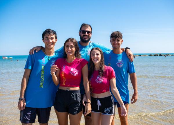 Groupe d'amis souriants à la plage avec des t-shirts colorés.